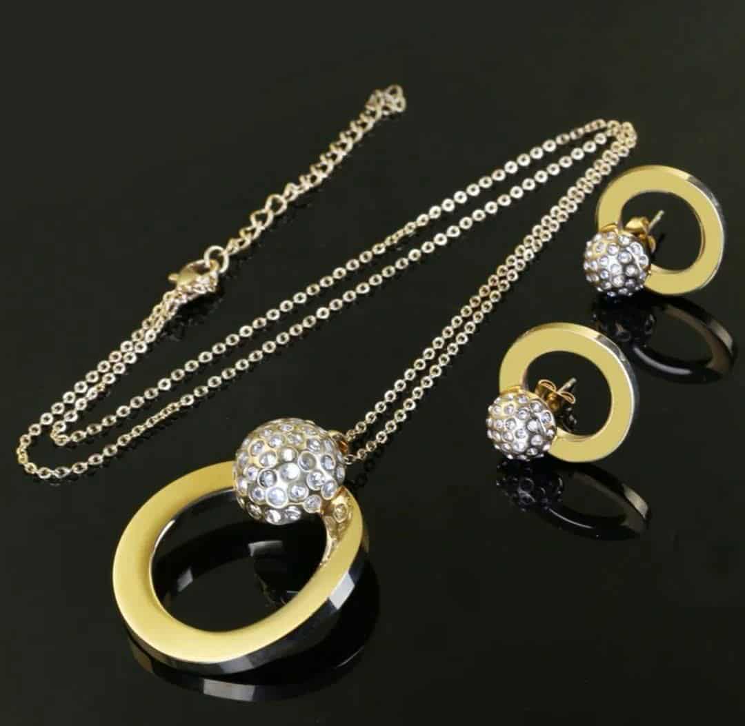 Hochwertiges Edelstahl-Set bestehend aus einer filigranen, goldenen Kette in Kreisform mit einer Kugel versehen mit zahlreichen Zirkonia und passenden Ohrsteckern in Kreis-Form. Langlebig, wasserfest, hypoallergen und alltagstauglich.