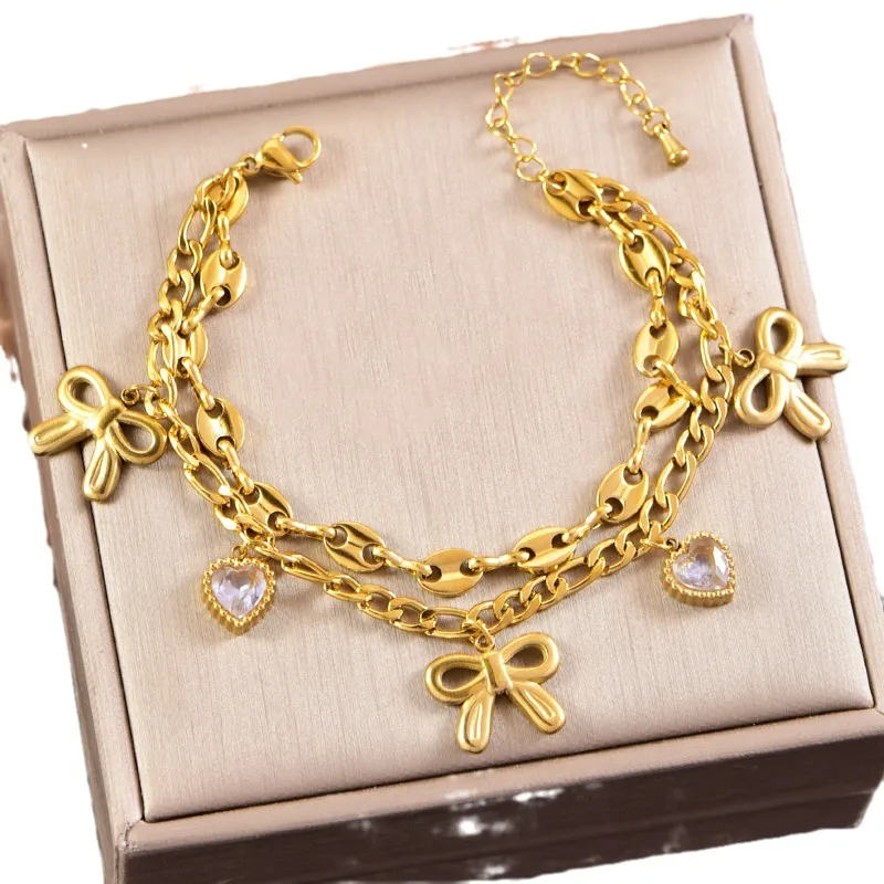 Hochwertiges Edelstahl-Armband, doppelreihig, in edlen goldenen, minimalistischen Schleifen und herzförmigen Zirkonia. Langlebig, wasserfest, hypoallergen und alltagstauglich.