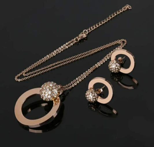 Hochwertiges Edelstahl-Set bestehend aus einer filigranen, goldenen Kette in Kreisform mit einer Kugel versehen mit zahlreichen Zirkonia und passenden Ohrsteckern in Kreis-Form. Langlebig, wasserfest, hypoallergen und alltagstauglich.